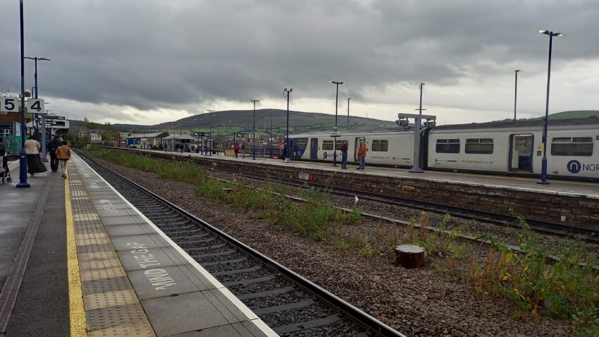 Scenic view of the hills from Stalybride station, a Northern train sits in the platform across the tracks.